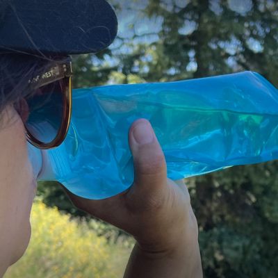 Woman drinking from a Vapur collapsible water bottle while on a hike.