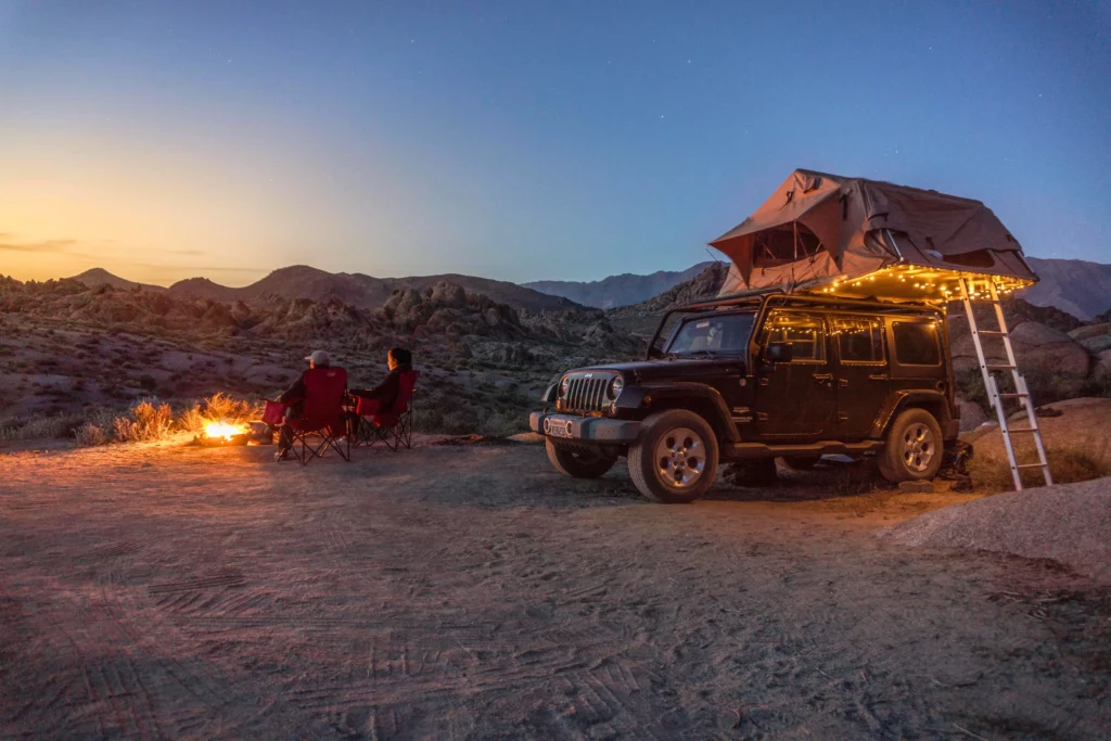 A couple sitting by a campfire next to their Jeep with a rooftop tent. camping for couples