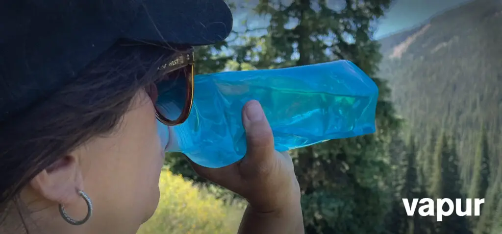 Woman drinking water from a Vapur collapsible water bottle while on a hike.