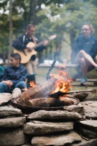 Dad playing guitar behind a family enjoying a campfire while camping.