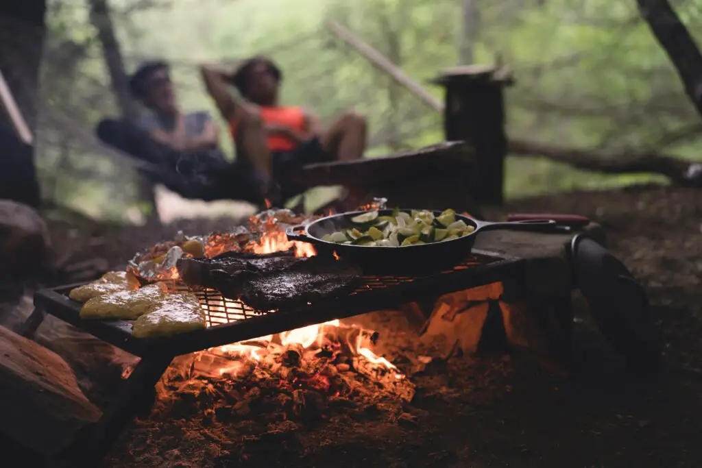 A couple cooking food over the campfire while camping.