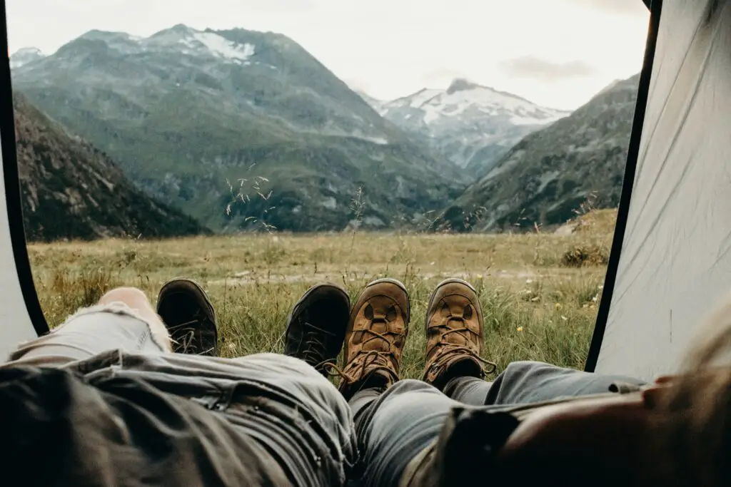 A couple laying down in a tent while looking past their feet to the surrounding mountains.